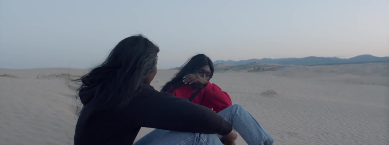 Two women sit in the sand in the desert and talk