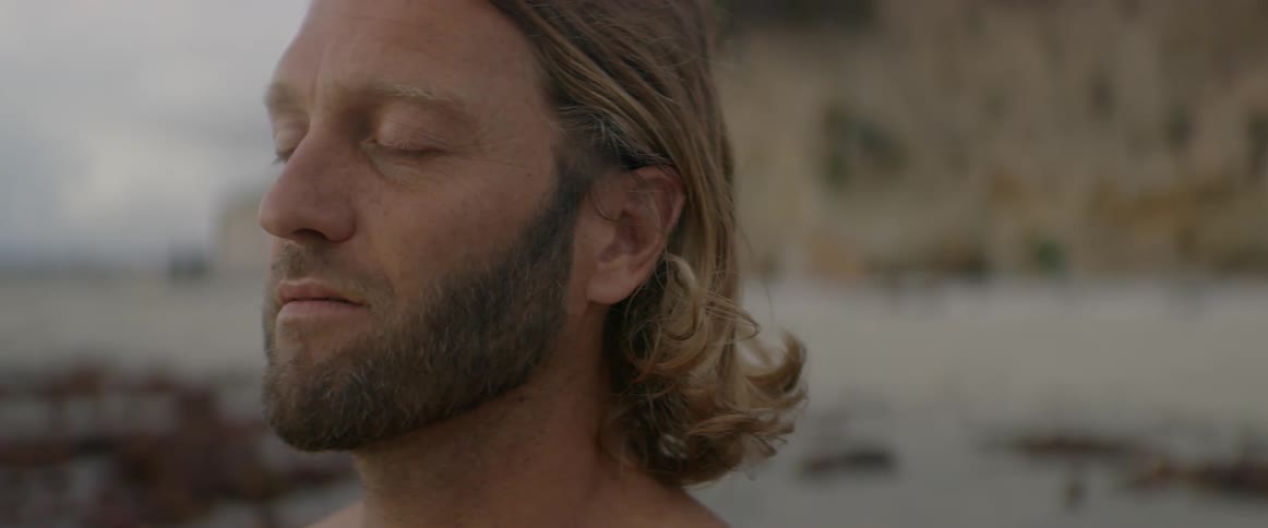A man stands serenely on a beach with his eyes closed