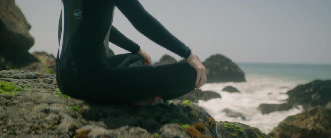 A man sits on a rock staring out at the ocean