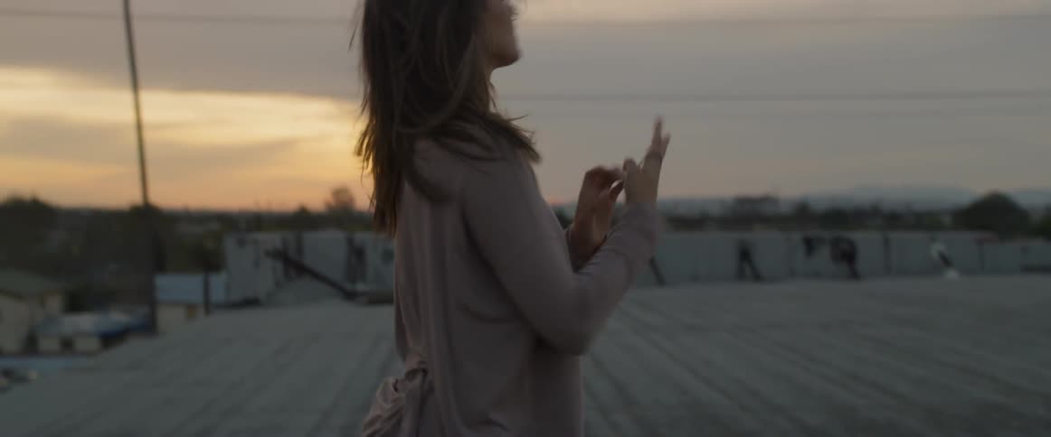 A female removes her bag and pulls her hair into a ponytail to avoid the wind outside