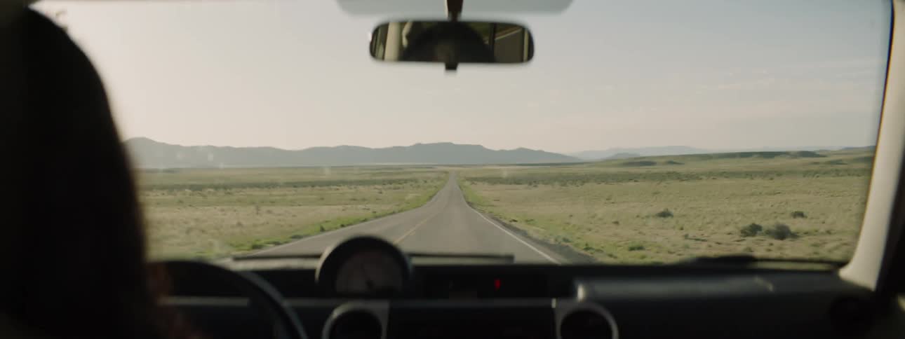 Someone drives down an empty road in the desert