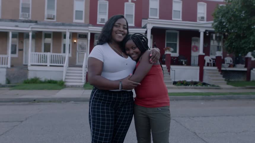 Two women hugs in a street in front of houses