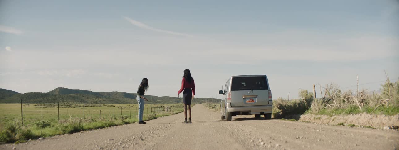Two woman walk along a dirt road next to a car they just exited