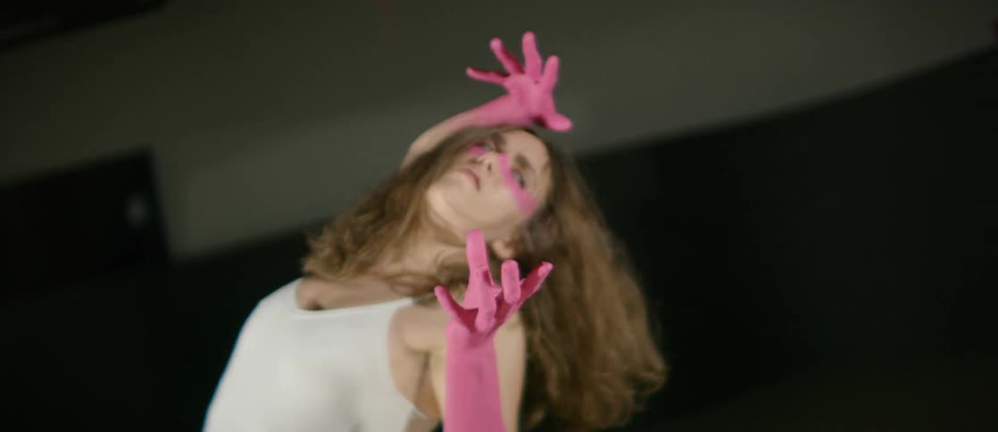 A woman with her forearms and hands painted pink does an interpretive dance in a spotlight