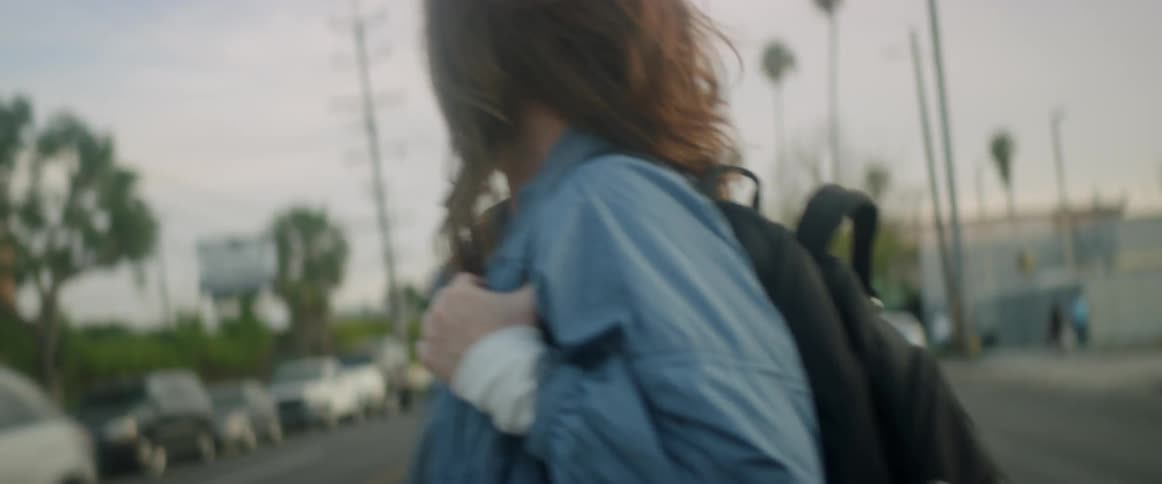 A woman with a backpack walks across the road in front of traffic