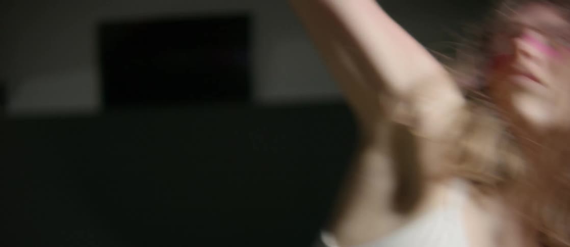 A woman with her forearms and hands painted pink does an interpretive dance in a spotlight