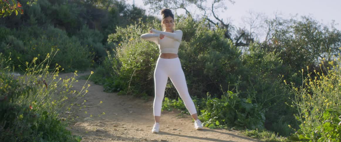 A woman stretches on a path surrounded by shrubs at sunrise