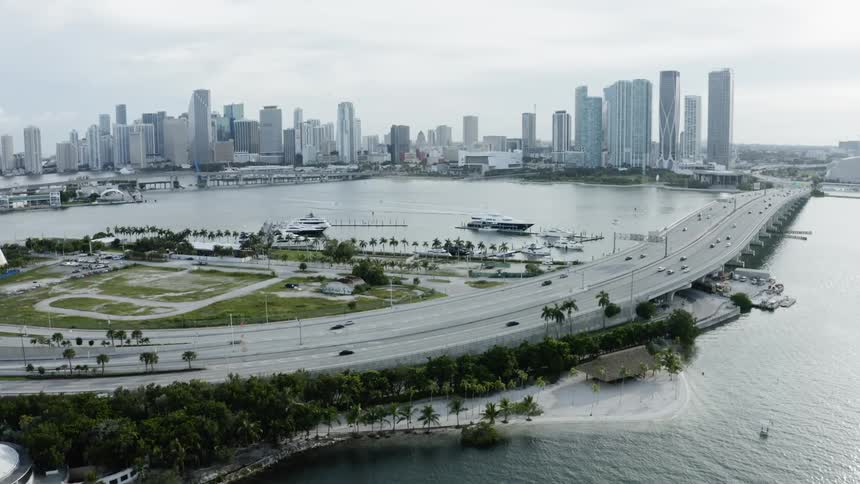 A lot of cars that are driving over a bridge in a city next to the ocean