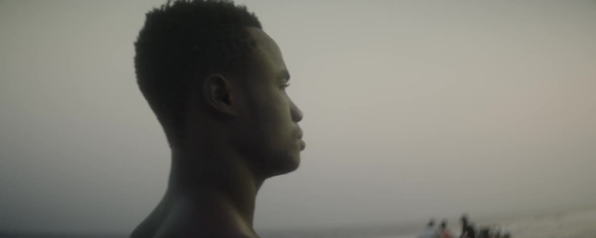 A man walks along near the ocean as people in the background stand on the beach