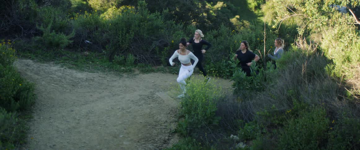 A group of woman jog up a hill on a dirt path with greenery to either side