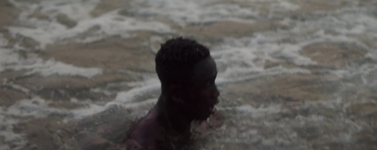 A man stands up to his shoulders in the ocean as waves flow by him