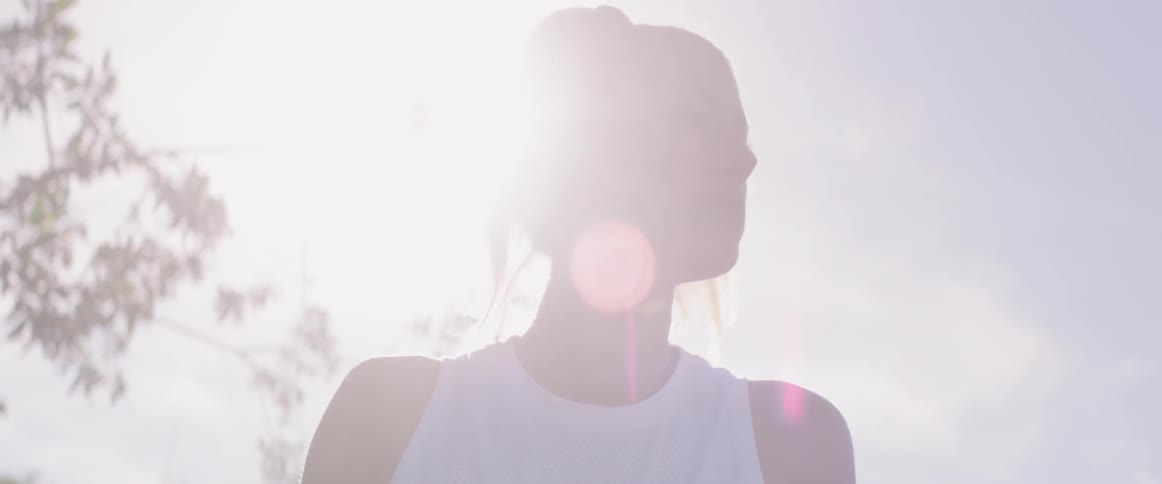 A woman stands in brilliant sunlight with a tree behind her