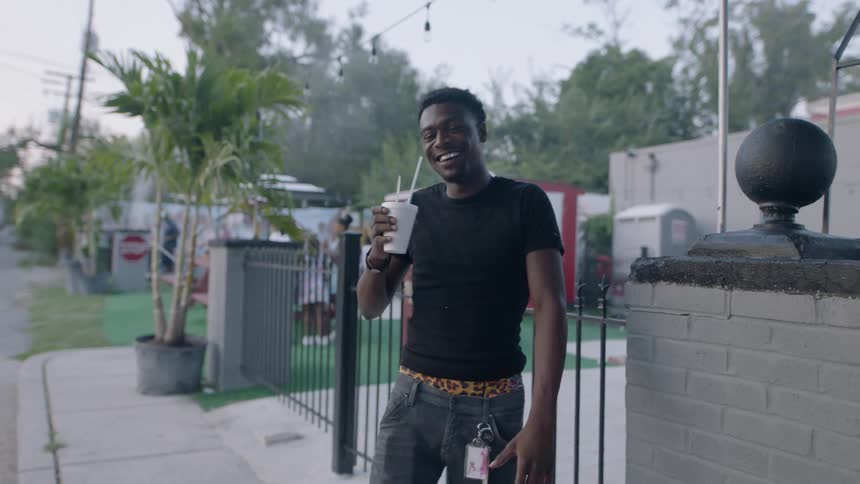 A man holding a shaved ice is dancing and swaying in a neighborhood in daylight