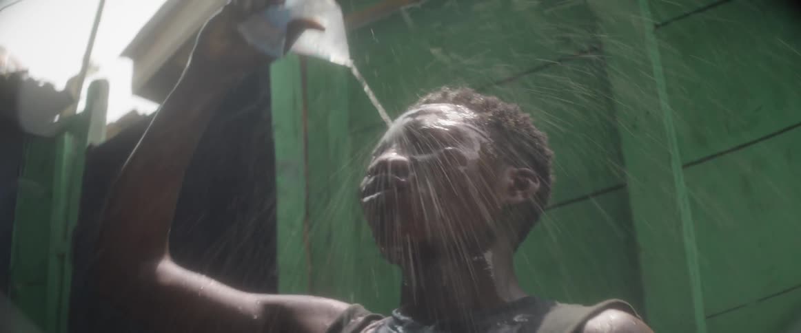 A man squirts water on his head and then takes a drink from the container