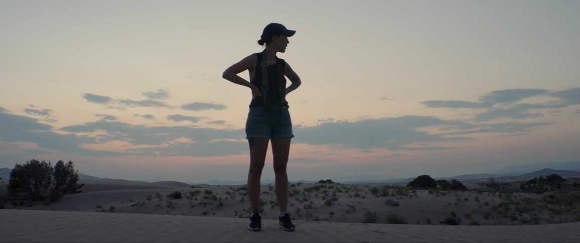 A woman in shorts and a tank top standing in the middle of the desert