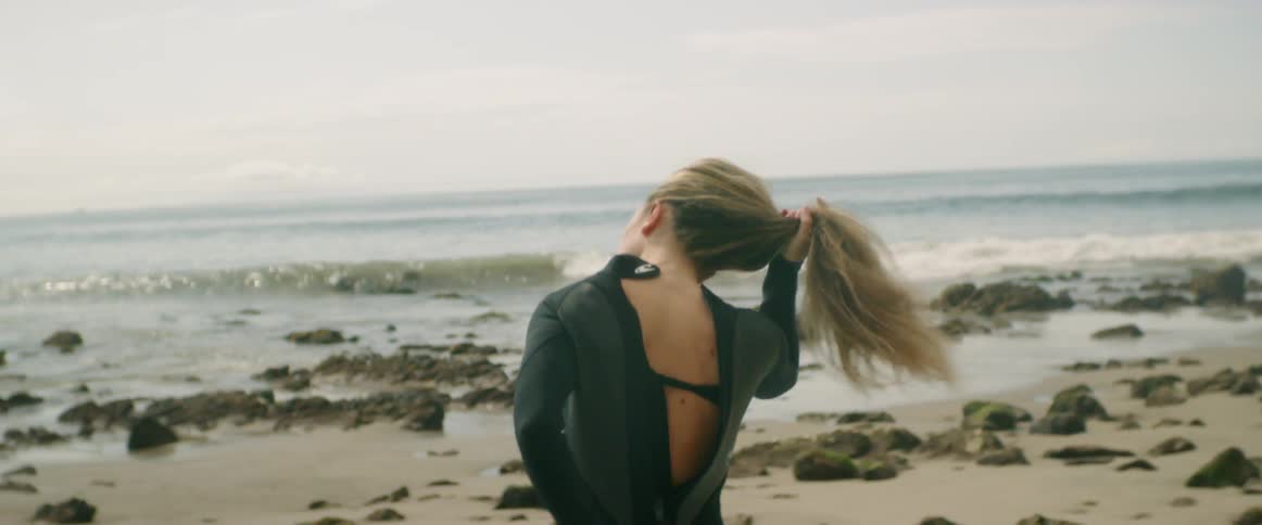 A woman puts on a wet suit on the beach