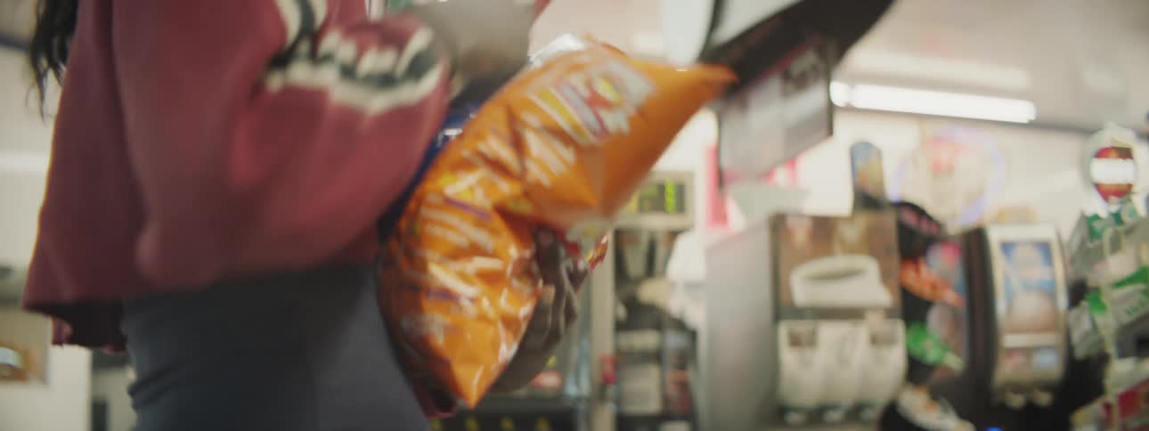 A woman grabs bags of chips from a grocery store shelf