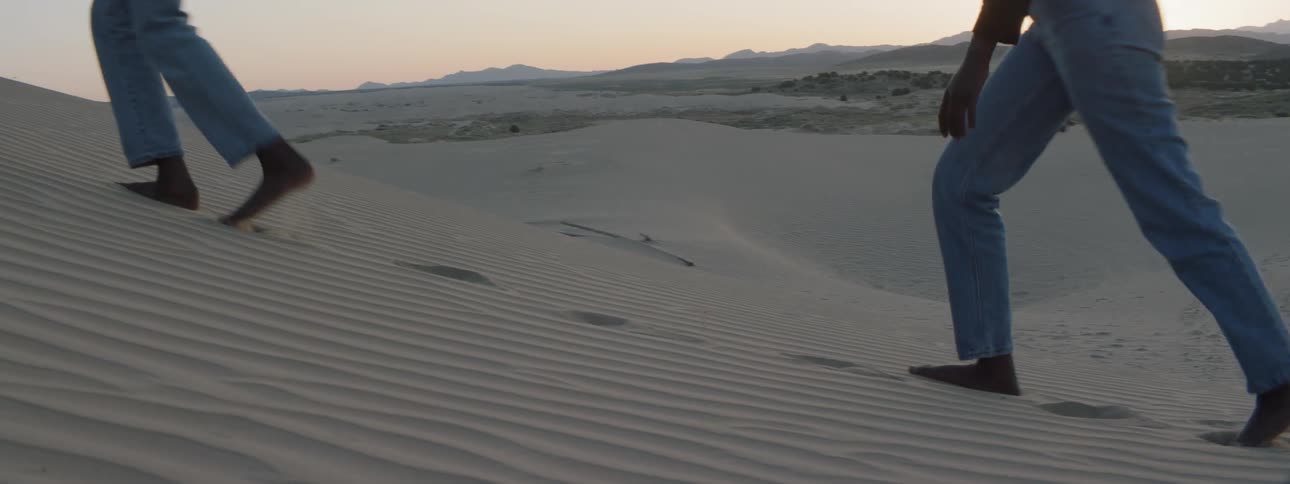 Two people walk through the desert with bare feet