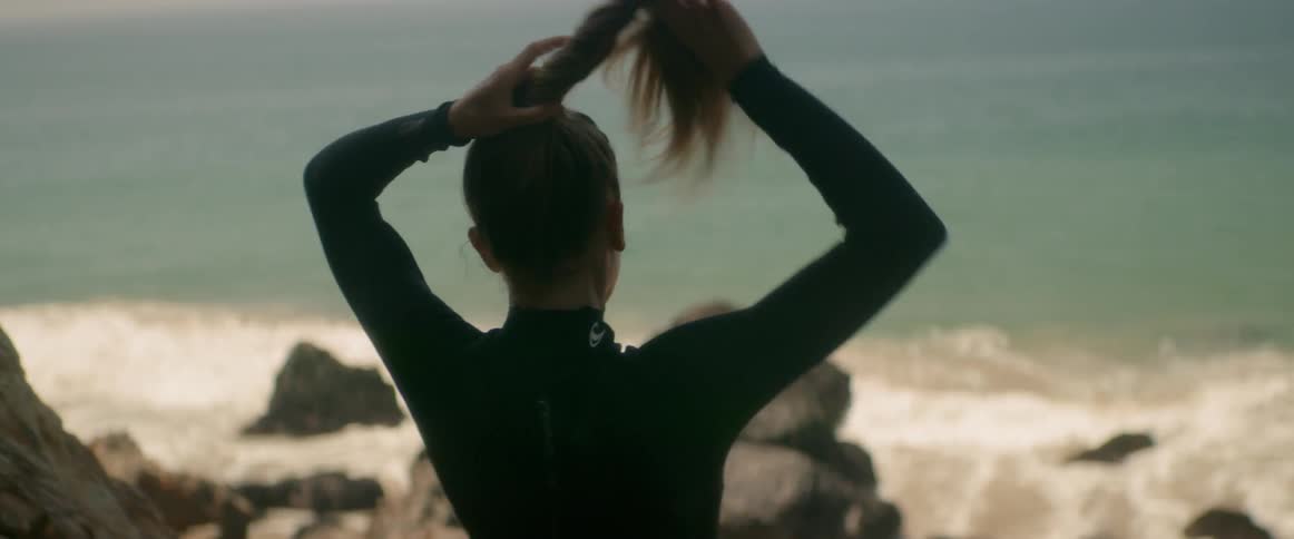 A woman puts her hair in a ponytail by the ocean