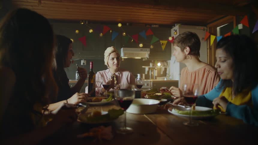 A group of five people eat and talk at a dinner table
