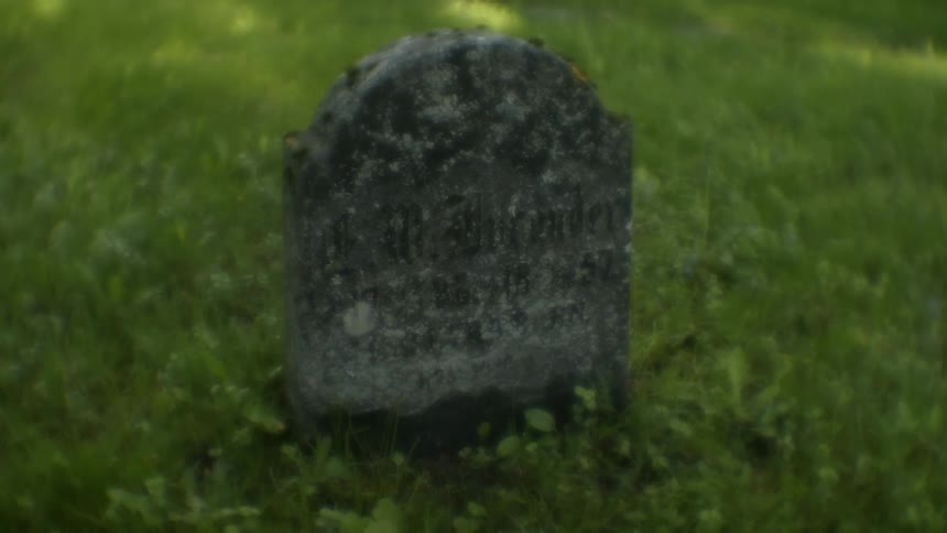 An old gravestone sitting in a grassy field