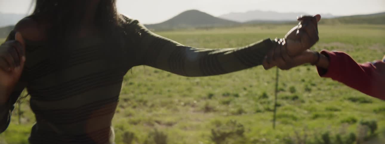 Two women fight in the middle of a huge grass field with mountains in the background