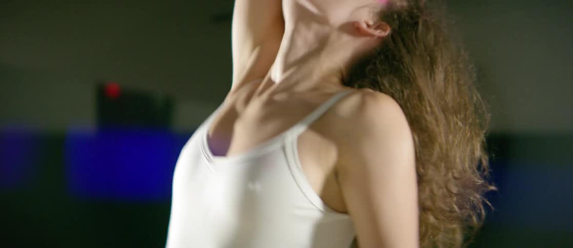 A woman with her forearms and hands painted pink does an interpretive dance in a spotlight
