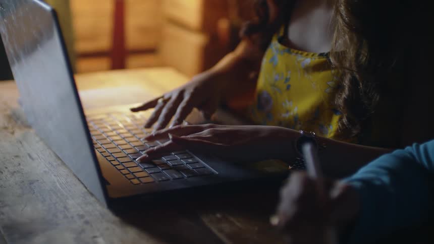 A woman types on a keyboard while a person next to her writes,