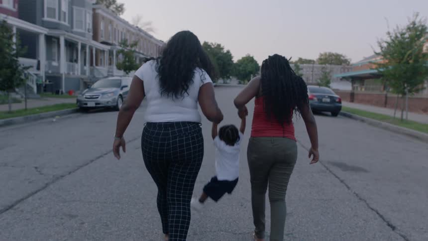 Two women walk down the street holding the hands of a toddler