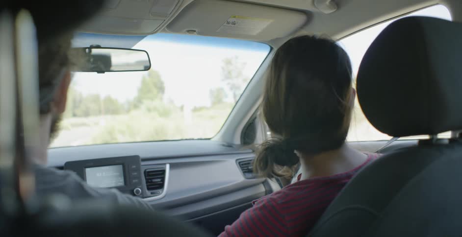 A man and woman driving in a car through the hills