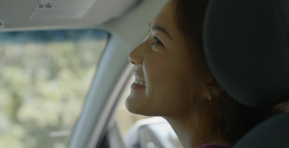 A woman in the passenger seat of a car smiles over at the driver