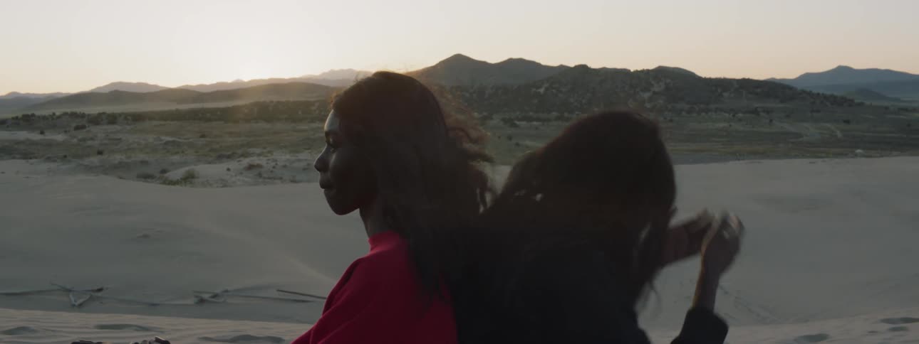 Two woman sit back to back on the beach