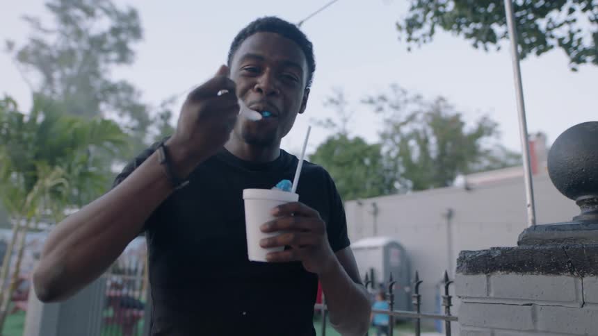 A man eating a snow cone on the sidewalk