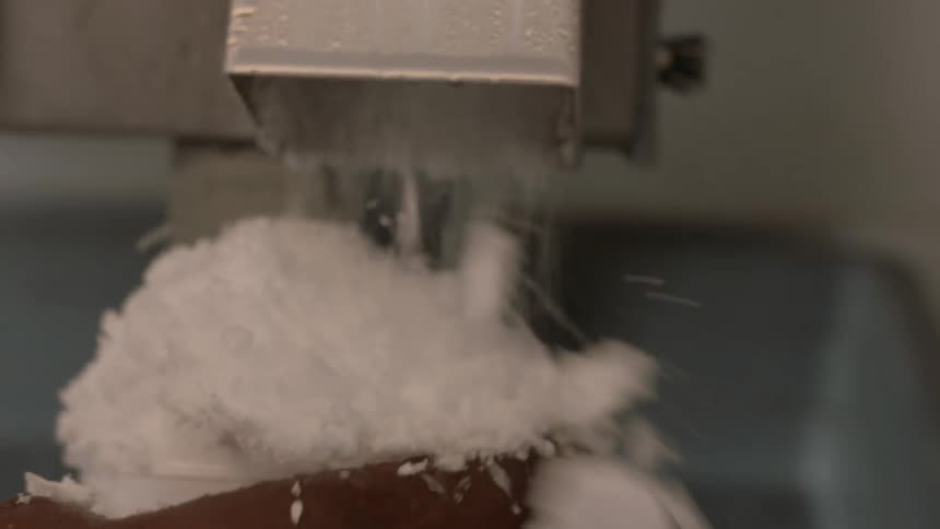 A person holds a cone as ice shavings are dispersed from a machine