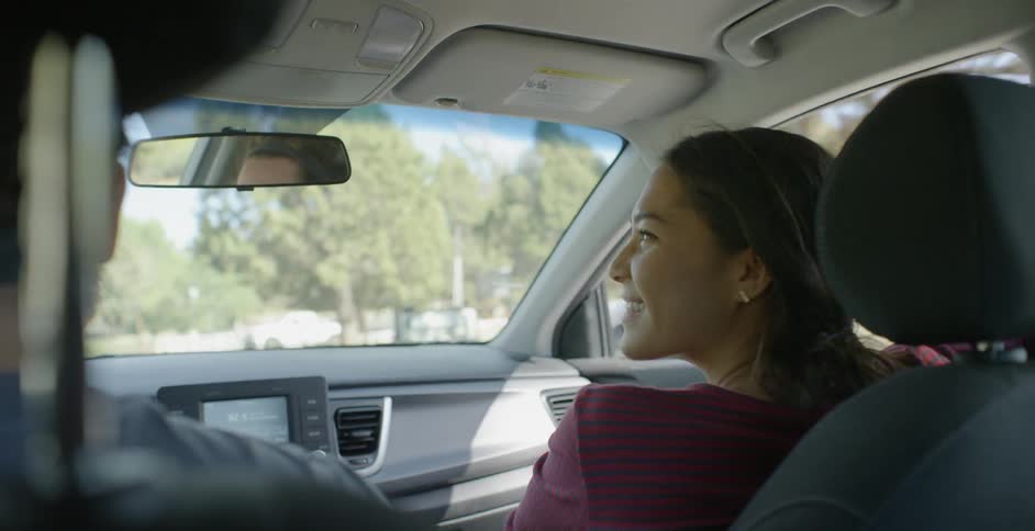 A woman in the passenger seat of a car smiles at the man that is driving
