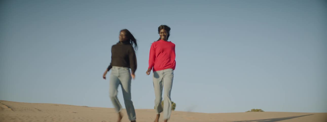 Two women holding hands and running through the desert