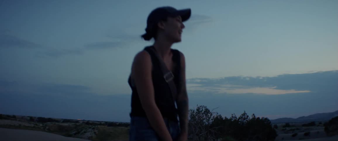 A woman in a tank top smiling walking around at dusk