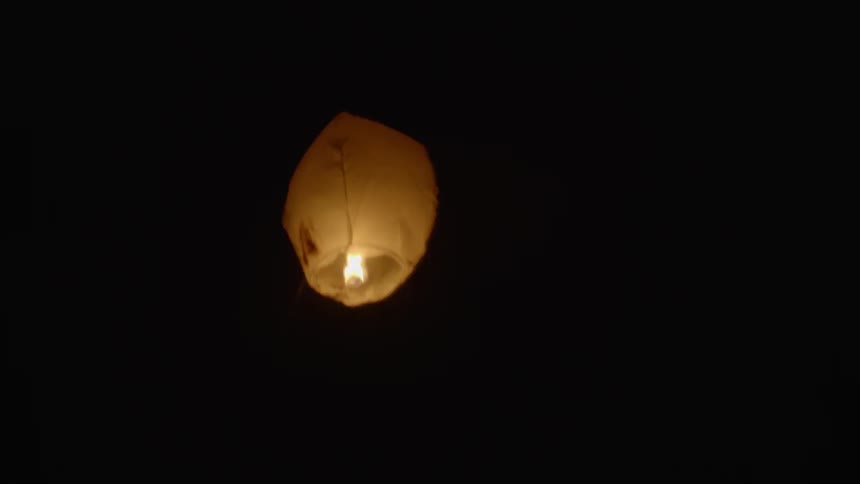 Flame shines brightly in a paper lantern that floats upwards in the dark