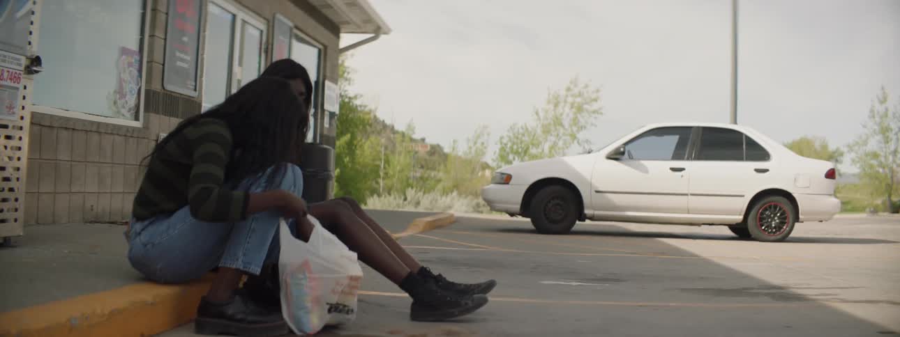 Two women sitting down on a curb with snacks