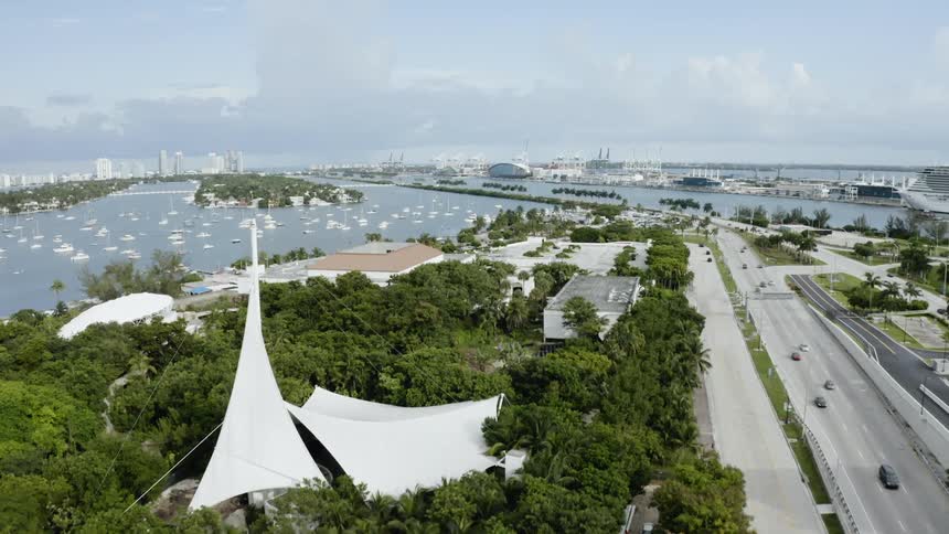 A body of water lays next to a patch of trees and a highway with cars going over it
