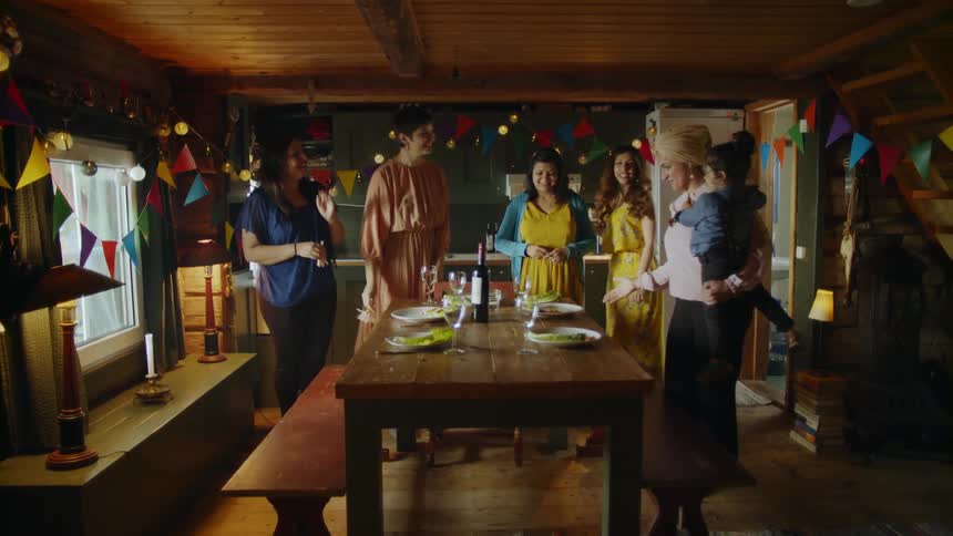 A group of people gather around a dining table and greet each other