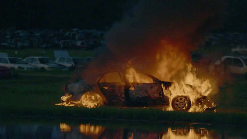 A car burns on the other side of a body of water in the darkness