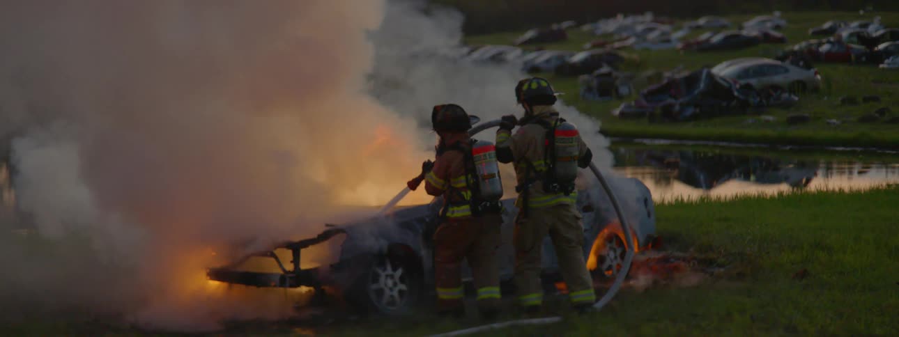 A pair of firefighters that are putting out a fire on a car