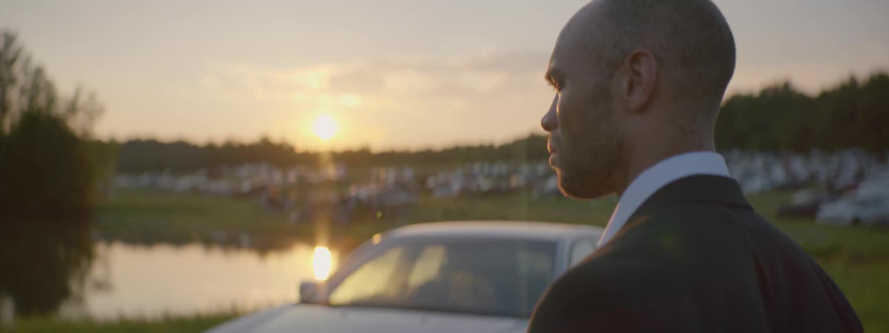 A man is looking toward a vehicle then stares off in another direction