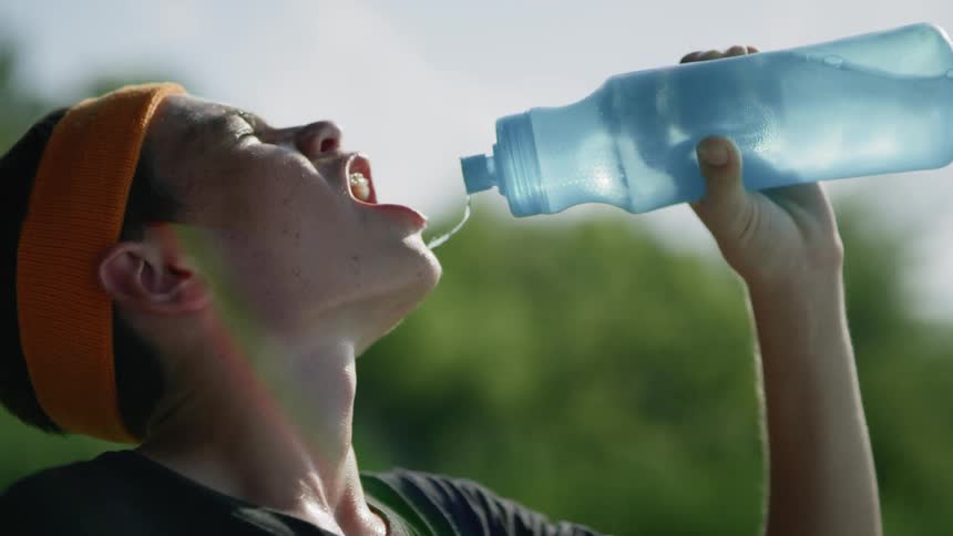 A boy squirts water out of a water bottle into his mouth