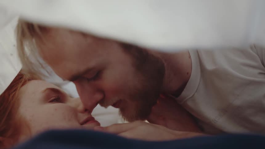 A man and woman kissing each other under sheets