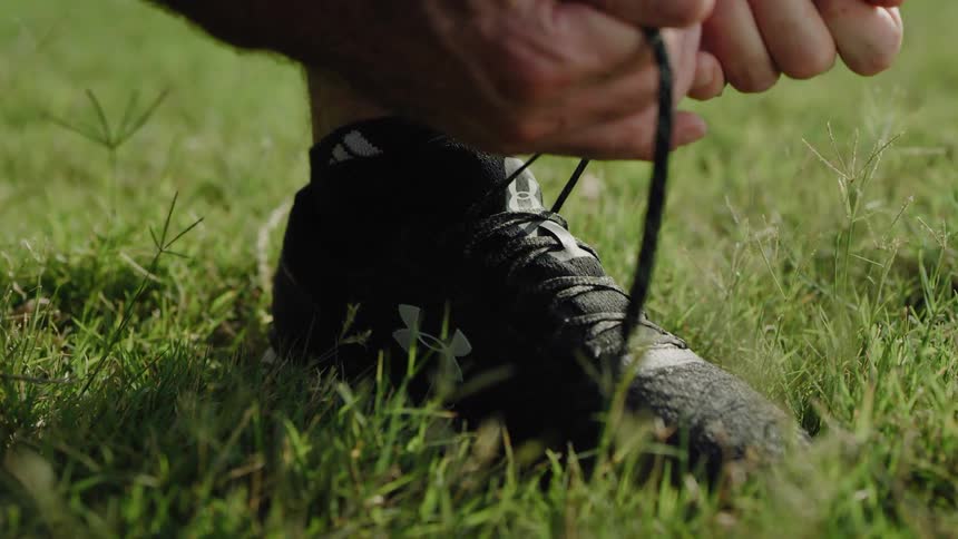 A man ties his shoe on a grass field