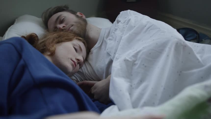 A man and a woman lay cuddling in a bed
