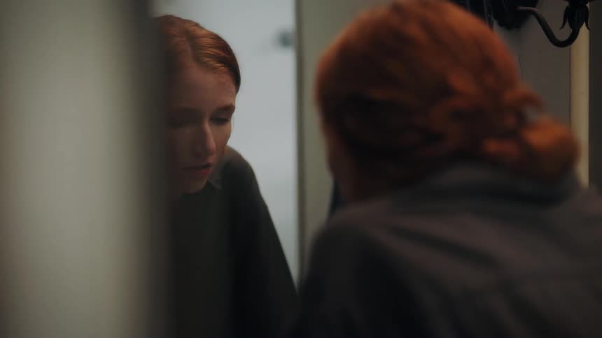 A woman looks into a mirror then bows her head