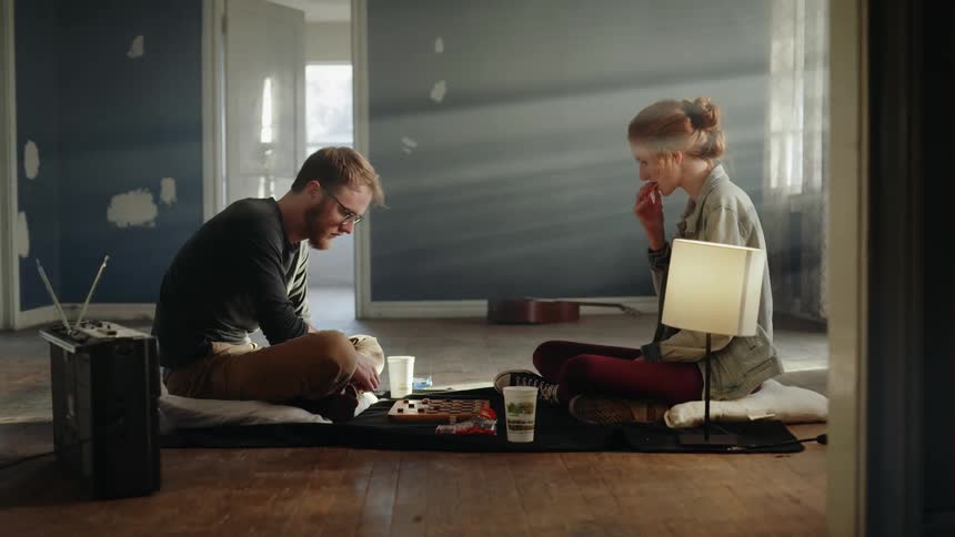 A man and a woman sit on the floor in the sunlight playing a board game